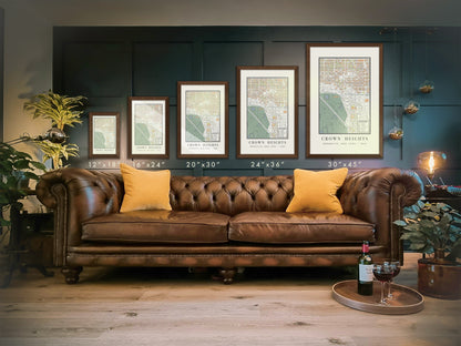 A visual guide comparing five vertical frame sizes for the 1908 Crown Heights map print, in sizes 12 by 18 inches, 16 by 24 inches, 20 by 30 inches, 24 by 36 inches, and 30 by 45 inches. The historic Brooklyn wall art is presented in solid brown oak frames on a dark paneled wall, situated over a brown leather chesterfield sofa.