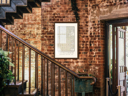 An 1880 archival map of East Williamsburg, Brooklyn, showcased in a solid dark oak frame. The restored vintage print is hung on a rugged exposed brick wall in an industrial entryway beside a metal and wood staircase.
