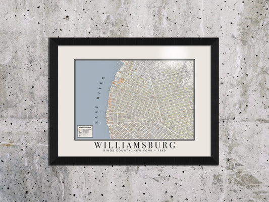 A museum-grade 1880 map of Williamsburg, Brooklyn, hanging against a distressed concrete wall. The vintage cartography print is enclosed in a solid black oak frame, adding an architectural element to an industrial-style room.