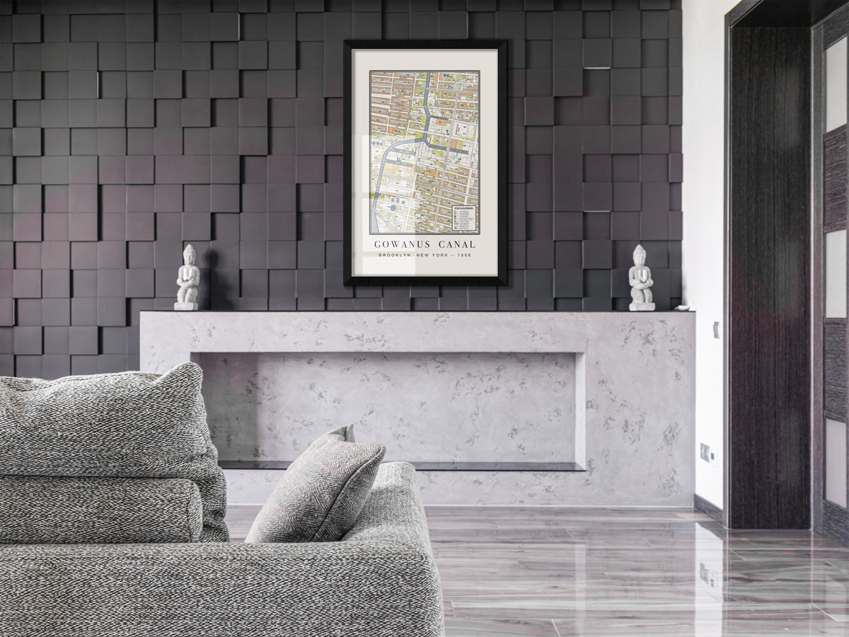 A 1908 archival map showing the Gowanus Canal in Brooklyn, housed in a solid black oak frame. The industrial vintage print hangs on a modern dark geometric wall, situated over a light grey sofa and a raw concrete mantle.