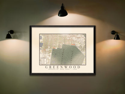 An archival 1908 map of Green-Wood Cemetery in Brooklyn, showcased in a solid black oak frame. The historic survey print is centered on a dimly lit, smooth wall, highlighted by three black industrial sconce lights.