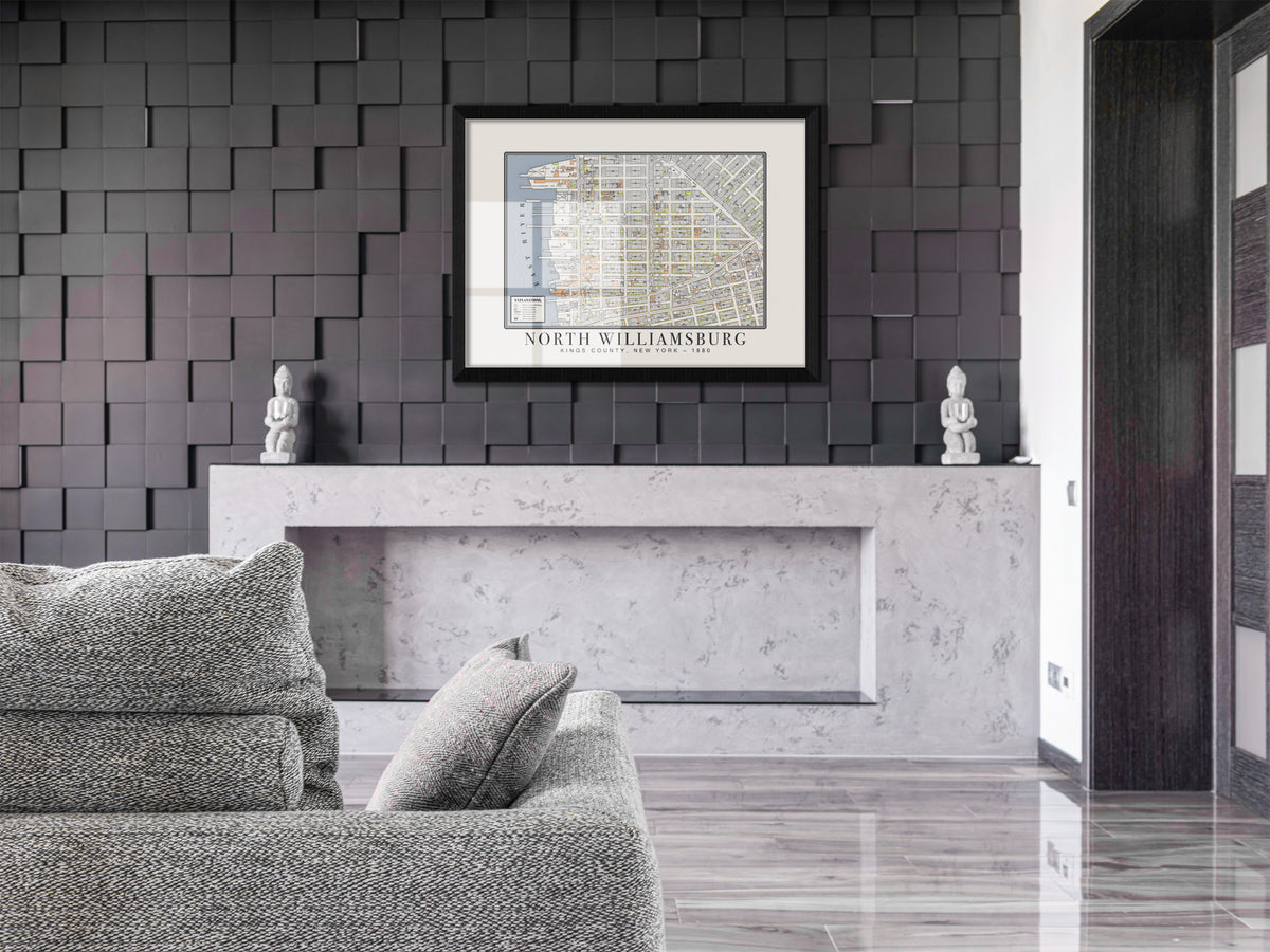 An archival 1880 map of North Williamsburg, Brooklyn, featured in a solid black oak frame. The vintage New York architectural print hangs on a dark 3D accent wall above a minimalist concrete mantle and a light grey textured couch.